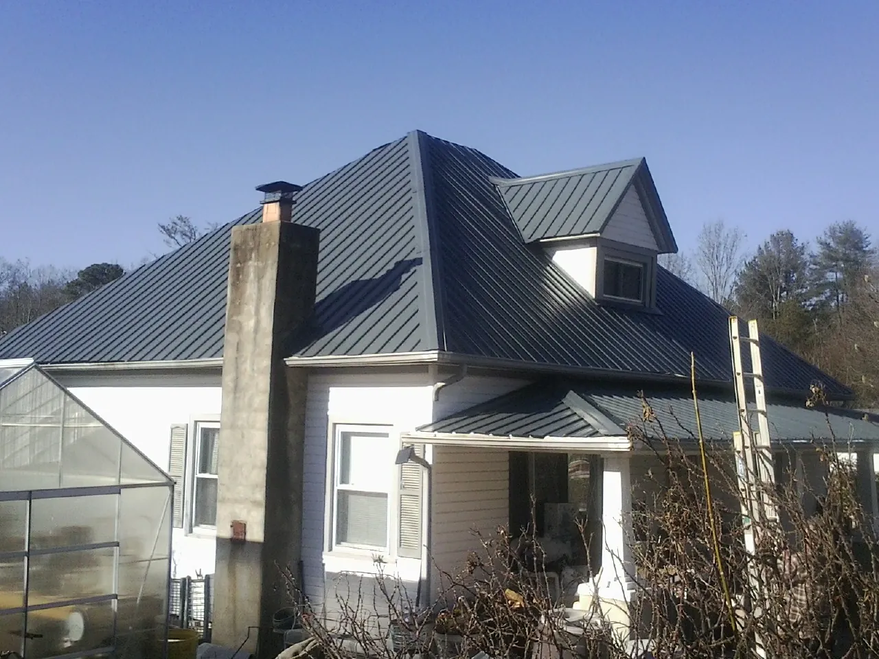 Dark blue standing seam metal roof on a white farmhouse with dormer — Slate & Tile Roof Repair by Roofing Brothers in Cusick