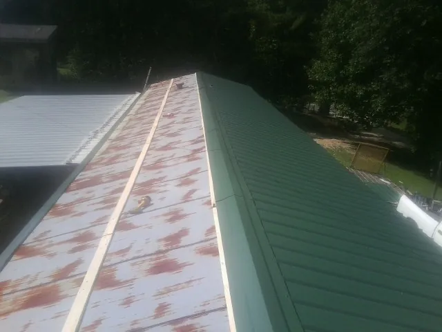 Old rusted panels beside newly installed green metal roofing — Wind Damage Roof Repair by Roofing Brothers in Cusick