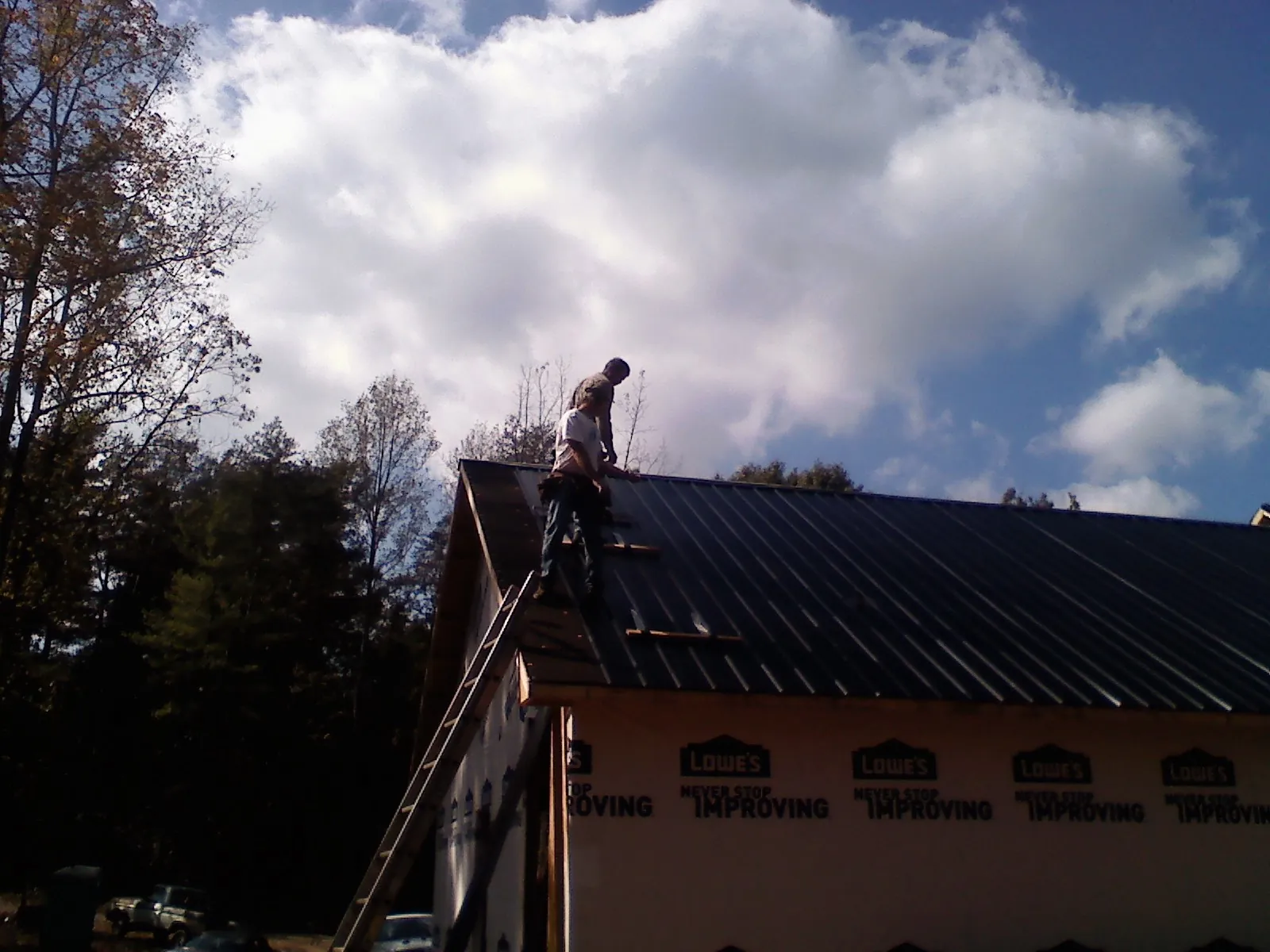 Roofer fastening dark metal panels high against a cloudy sky, from a Roof Inspection job in Cusick